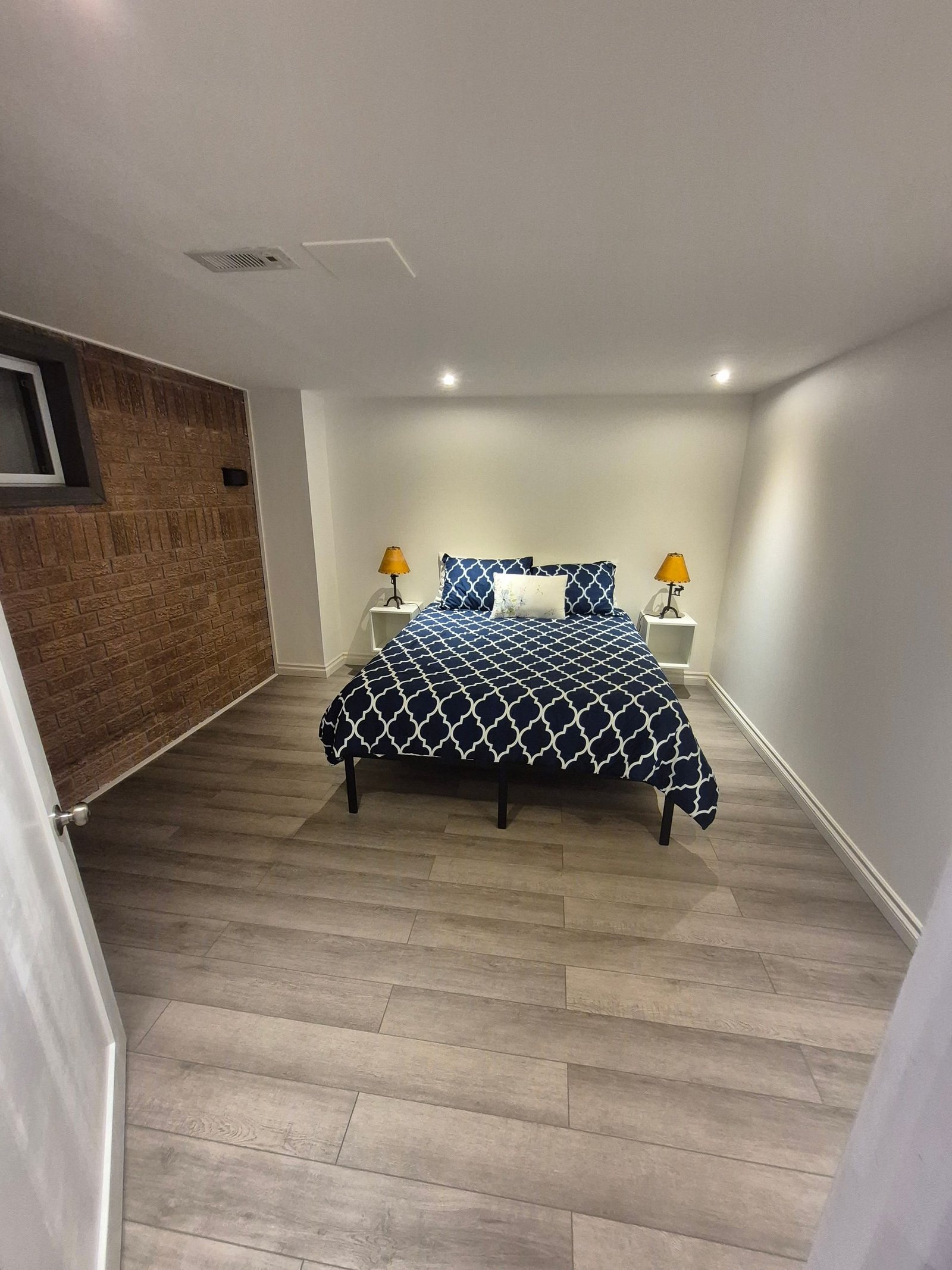 Bedroom 1 with a queen bed, bedside lamps, and a brick accent wall